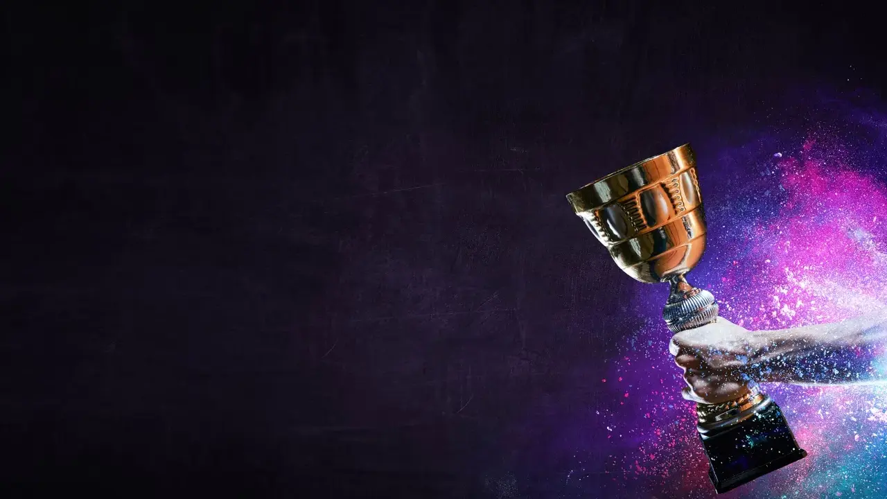Une main tient un trophée doré, entouré de poussière colorée. La musique pour annoncer un gagnant résonne.