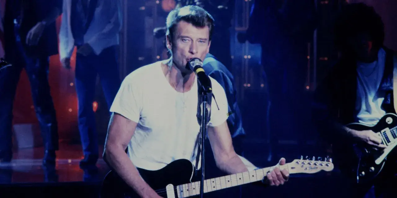 Johnny Hallyday chante en live, guitare à la main. On se demande combien gagne un musicien de Johnny Hallyday pour une telle performance.