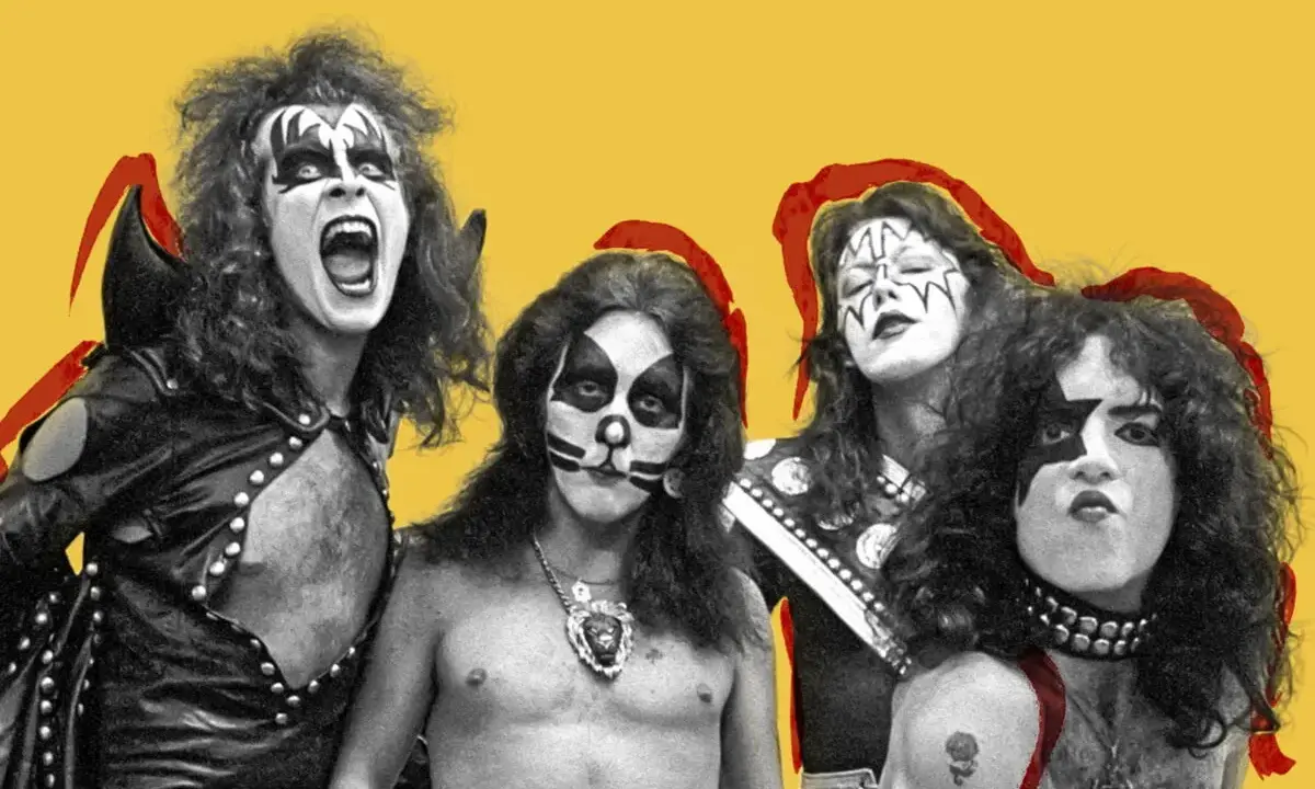 Le groupe Kiss, avec leurs maquillages iconiques, pose sur fond jaune. Un des membres hurle, prêt à enflammer la scène.