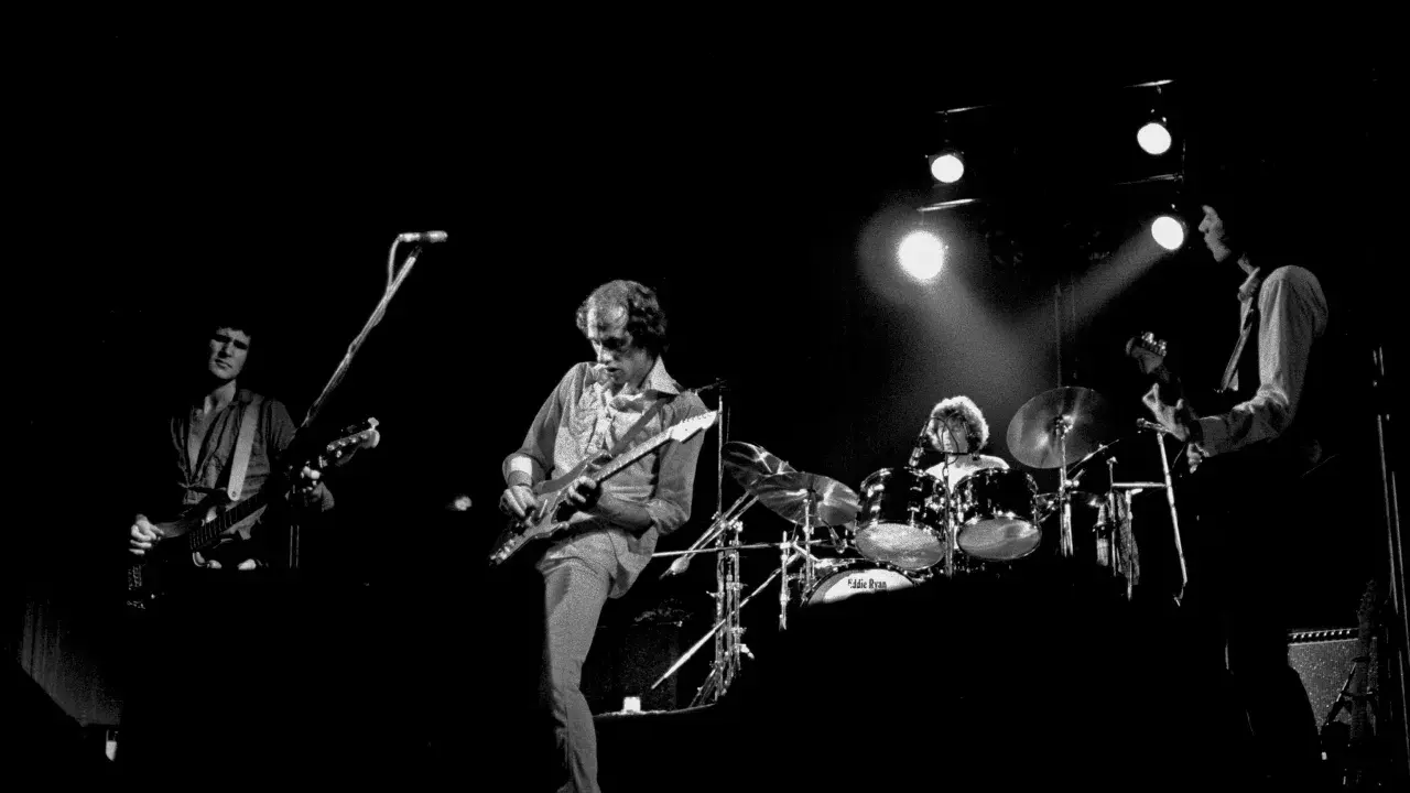 Quatre musiciens sur scène, guitares et batterie. Un aperçu de la **dire straits discography** en live.
