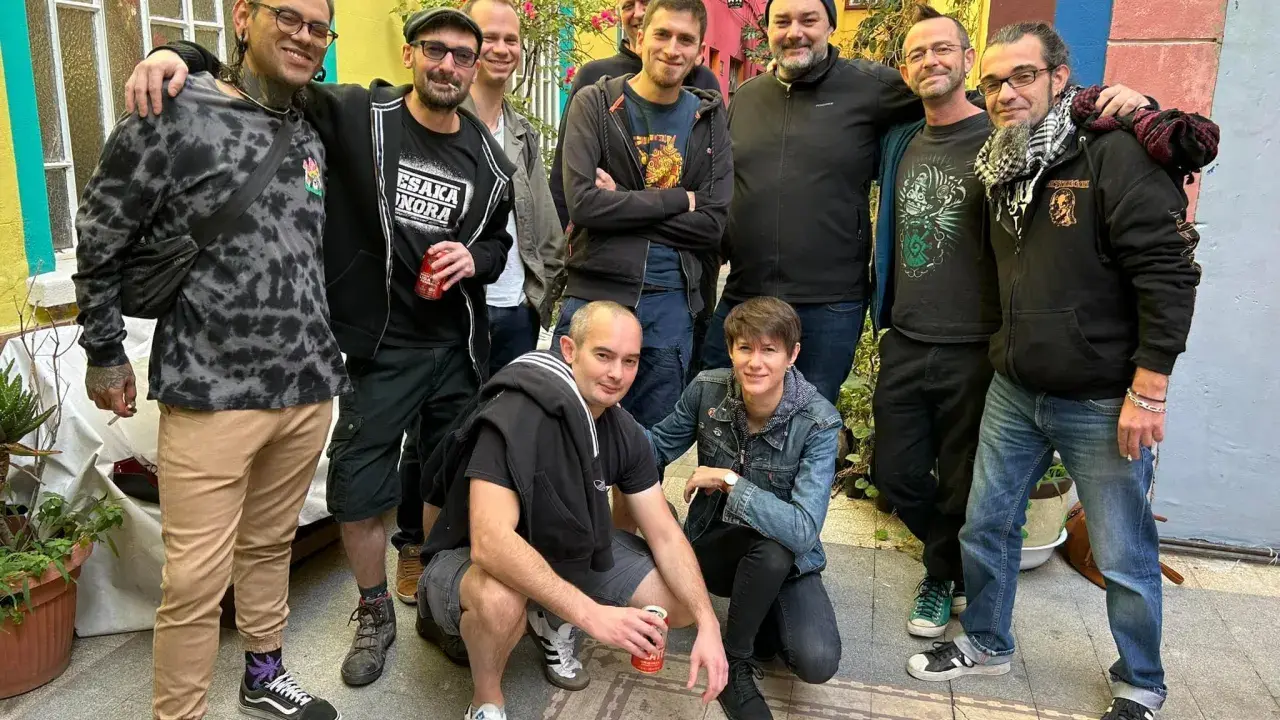 Un groupe d'amis, dont certains portent des t-shirts avec des motifs ska p, pose joyeusement dans une ruelle colorée.