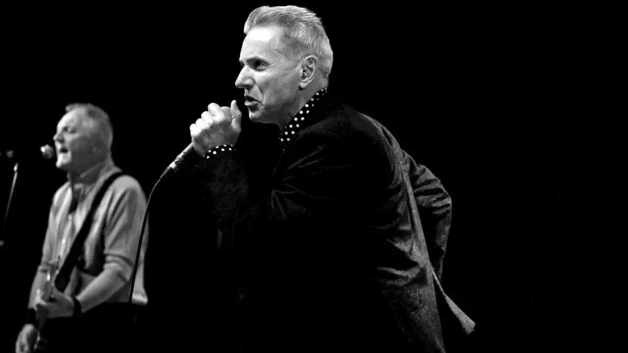 Le chanteur, comme un Dr Feelgood, captive la foule avec sa voix puissante. Un guitariste l'accompagne sur scène.