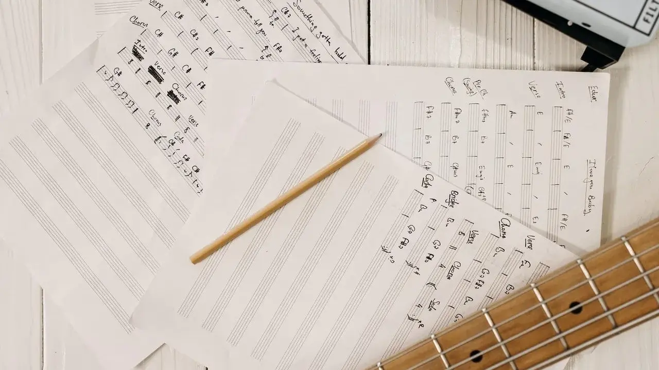 Feuilles de musique manuscrites, un crayon et une guitare. Le matériel parfait pour trouver l'inspiration pour écrire une chanson.