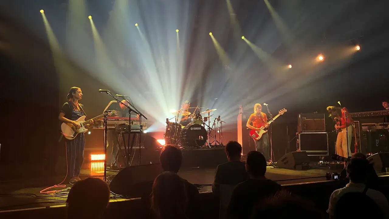 Une goat girl joue de la guitare sur scène, éclairée par des projecteurs.