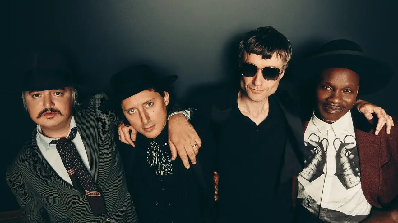 Quatre hommes stylés, comme des libertins modernes, posent ensemble. L'un porte un chapeau et une veste rayée, un autre un chapeau noir et une chemise à jabot. Le troisième, lunettes de soleil, est en noir. Le dernier, chapeau et veste bordeaux, arbore...