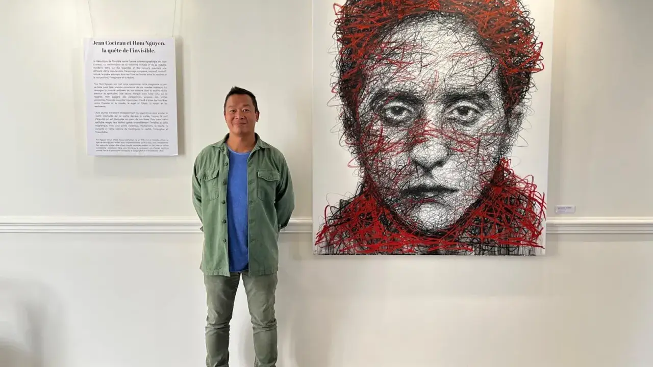 Un homme pose devant un portrait abstrait de Jean Cocteau, une œuvre de Hom Nguyen. La liste nom d'artiste est visible sur le mur.