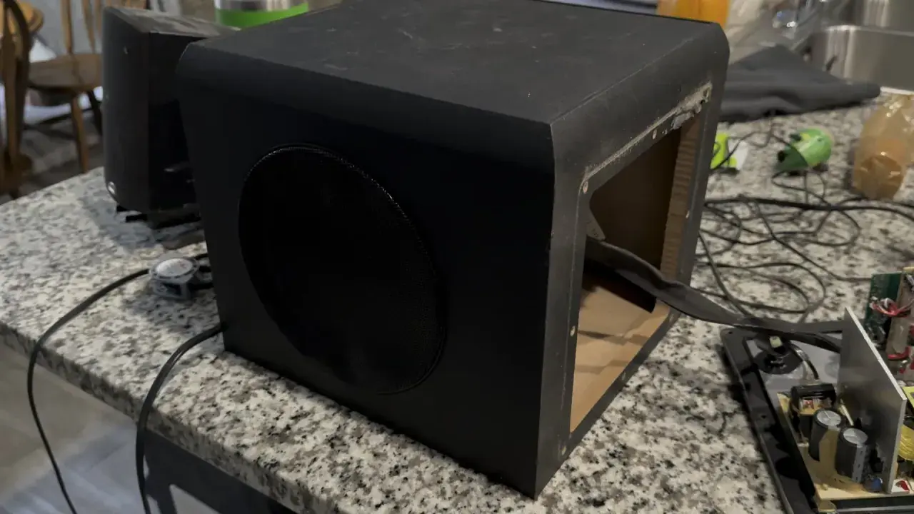 Un caisson de basse noir ouvert sur une table. Pour savoir si un caisson de basse fonctionne, vérifiez les connexions et le circuit imprimé.
