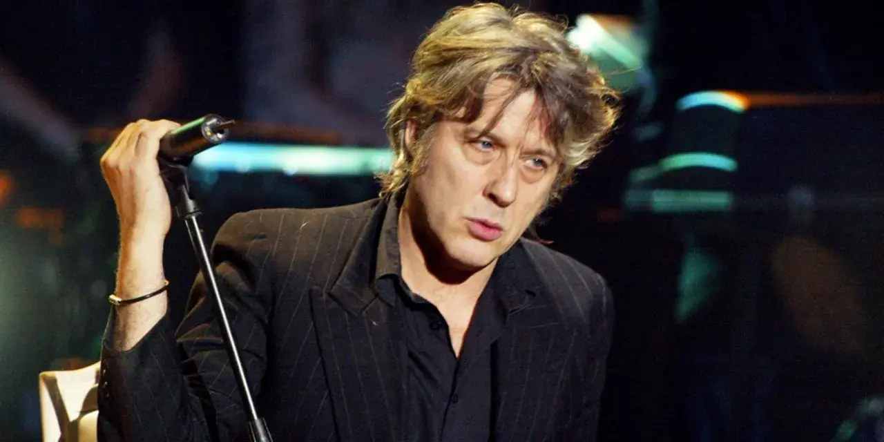 Arno, chanteur à la voix rocailleuse, tient un micro sur scène, le regard intense.