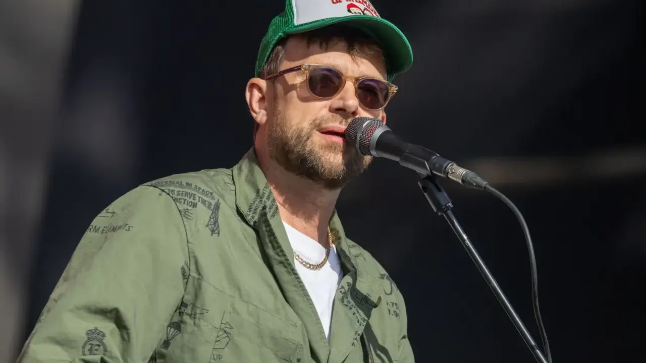 Damon Albarn, chanteur du groupe Gorillaz, porte une casquette et une veste verte ornée de motifs.