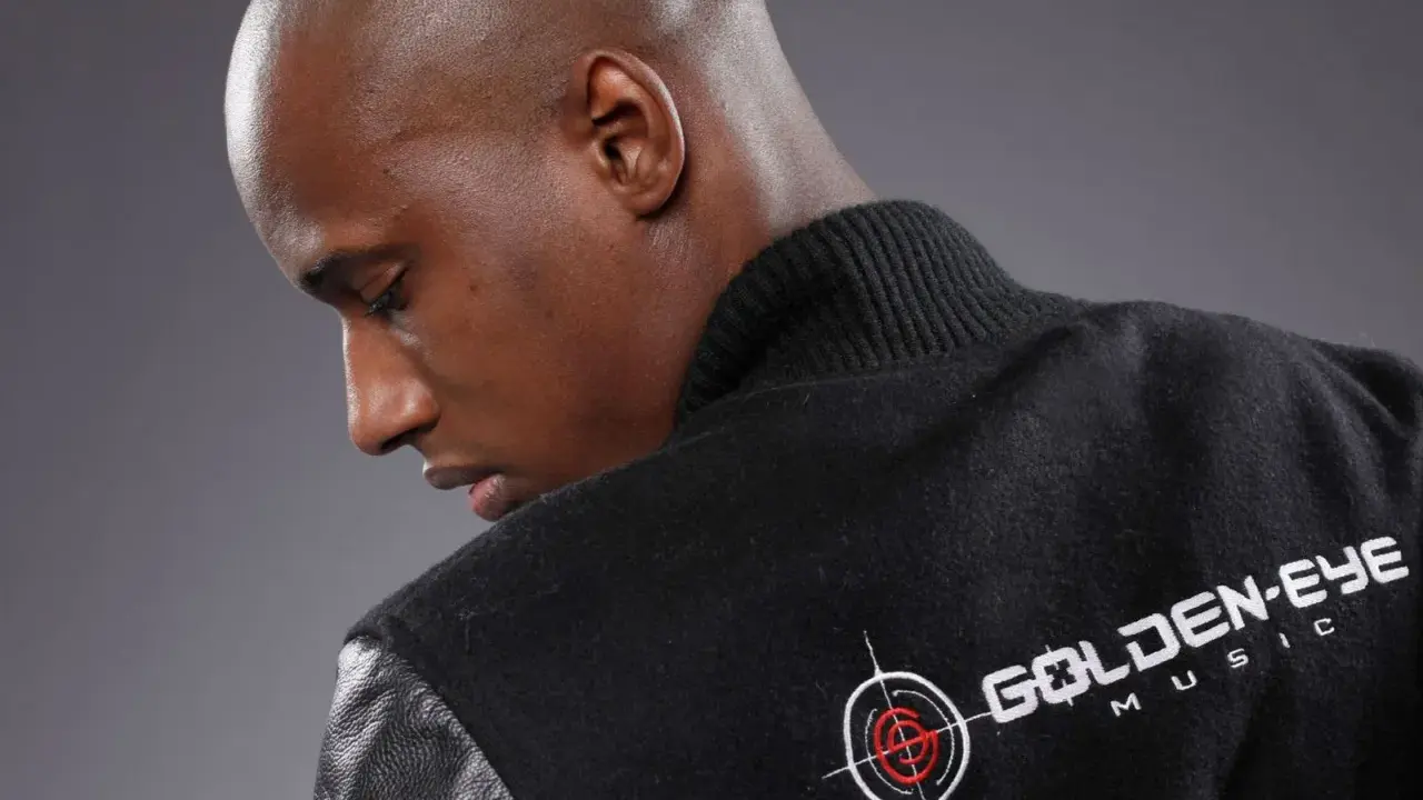 Un homme chauve porte une veste noire avec le logo "Golden Eye Music". Il est prêt à faire le buzz avec sa musique.