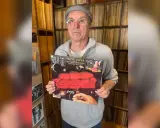 Un homme tient la pochette de l'album "One Size Fits All" de Frank Zappa, entouré de vinyles.