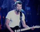 Johnny Hallyday chante en live, guitare à la main. On se demande combien gagne un musicien de Johnny Hallyday pour une telle performance.