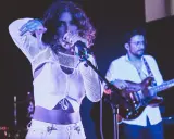 Une chanteuse au look audacieux, micro en main, semble exprimer son dédain pour une chanson nulle. Un guitariste l'accompagne sur scène.