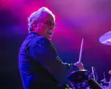 Le batteur Bruce Springsteen, concentré, frappe la caisse claire sous des lumières violettes et roses.