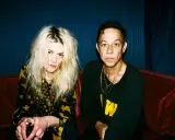Un couple, aux allures rock, pose sur un canapé rouge. Elle, aux cheveux blonds décoiffés, porte une robe à étoiles. Lui, au regard intense, arbore un sweat noir. Ils semblent vouloir "kill the young" par leur style.
