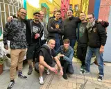 Un groupe d'amis, dont certains portent des t-shirts avec des motifs ska p, pose joyeusement dans une ruelle colorée.