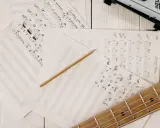 Feuilles de musique manuscrites, un crayon et une guitare. Le matériel parfait pour trouver l'inspiration pour écrire une chanson.