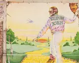 Elton John, sur la couverture du meilleur album Elton John, marche sur la route de briques jaunes vers un paysage idyllique.