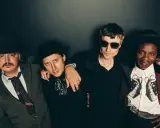 Quatre hommes stylés, comme des libertins modernes, posent ensemble. L'un porte un chapeau et une veste rayée, un autre un chapeau noir et une chemise à jabot. Le troisième, lunettes de soleil, est en noir. Le dernier, chapeau et veste bordeaux, arbore...