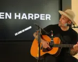 Ben Harper, chapeau sur la tête, joue de la guitare devant un écran affichant son nom et "Les Vies du Parisien".