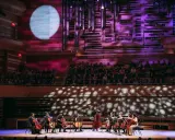 Un orchestre joue sur scène, éclairé par une lune projetée. C'est quoi un single ? Une pièce musicale unique, comme un solo d'un musicien.