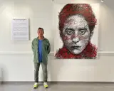 Un homme pose devant un portrait abstrait de Jean Cocteau, une œuvre de Hom Nguyen. La liste nom d'artiste est visible sur le mur.