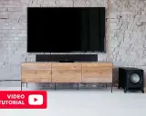 Un salon moderne avec une TV, une barre de son et un **pre out subwoofer** noir sur un meuble en bois.