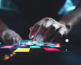 Main d'une personne naviguant sur une tablette avec des icônes colorées, suggérant une appli pour faire de la musique.