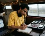 Artiste musicien, concentré sur son carnet, prépare sa demande de subvention artiste musique. Son studio mobile est prêt.