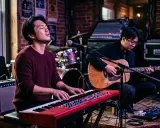 Deux musiciens jouent sur scène. L'un au piano rouge, l'autre à la guitare acoustique. Parfait pour un blog musique.