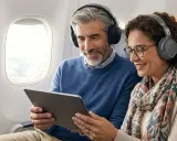 Couple souriant dans un avion, partageant une tablette et des écouteurs. Apprenez comment connecter deux appareils Bluetooth en même temps pour un voyage agréable.