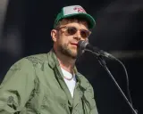 Damon Albarn, chanteur du groupe Gorillaz, porte une casquette et une veste verte ornée de motifs.