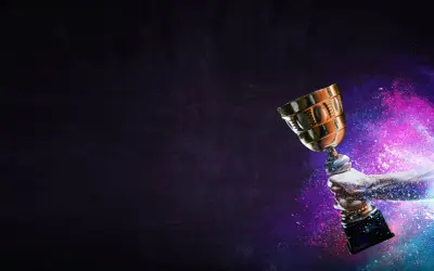 Une main tient un trophée doré, entouré de poussière colorée. La musique pour annoncer un gagnant résonne.