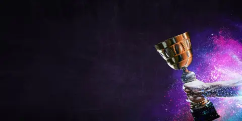 Une main tient un trophée doré, entouré de poussière colorée. La musique pour annoncer un gagnant résonne.