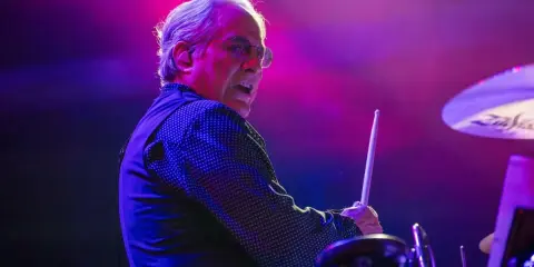 Le batteur Bruce Springsteen, concentré, frappe la caisse claire sous des lumières violettes et roses.