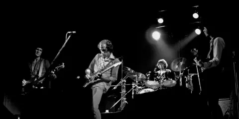 Quatre musiciens sur scène, guitares et batterie. Un aperçu de la **dire straits discography** en live.