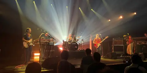 Une goat girl joue de la guitare sur scène, éclairée par des projecteurs.