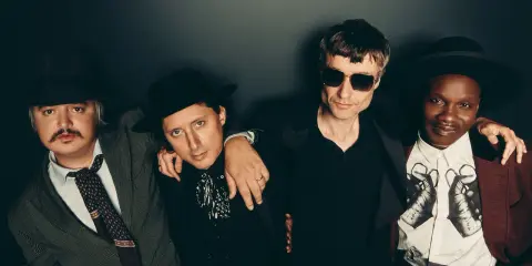Quatre hommes stylés, comme des libertins modernes, posent ensemble. L'un porte un chapeau et une veste rayée, un autre un chapeau noir et une chemise à jabot. Le troisième, lunettes de soleil, est en noir. Le dernier, chapeau et veste bordeaux, arbore...