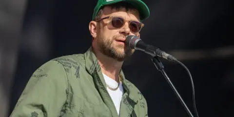Damon Albarn, chanteur du groupe Gorillaz, porte une casquette et une veste verte ornée de motifs.