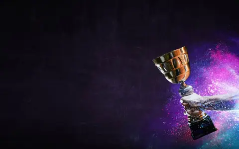 Une main tient un trophée doré, entouré de poussière colorée. La musique pour annoncer un gagnant résonne.