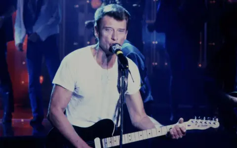 Johnny Hallyday chante en live, guitare à la main. On se demande combien gagne un musicien de Johnny Hallyday pour une telle performance.