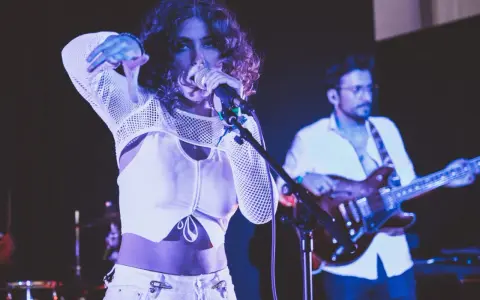 Une chanteuse au look audacieux, micro en main, semble exprimer son dédain pour une chanson nulle. Un guitariste l'accompagne sur scène.