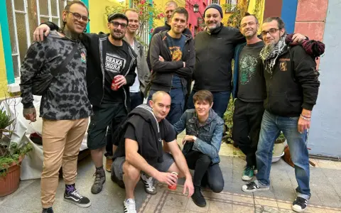 Un groupe d'amis, dont certains portent des t-shirts avec des motifs ska p, pose joyeusement dans une ruelle colorée.