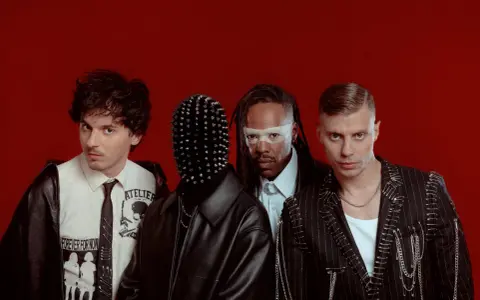 Les membres de Skip the Use posent sur fond rouge, avec des looks audacieux et stylisés.