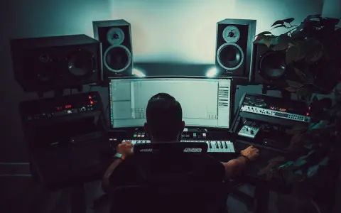 Un producteur de musique travaille dans son studio, entouré d'enceintes et d'équipements audio. Il manipule une interface logicielle, peut-être pour un projet avec un isrc code.