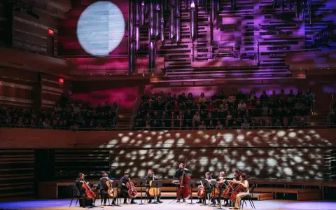 Un orchestre joue sur scène, éclairé par une lune projetée. C'est quoi un single ? Une pièce musicale unique, comme un solo d'un musicien.