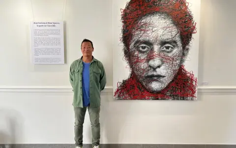 Un homme pose devant un portrait abstrait de Jean Cocteau, une œuvre de Hom Nguyen. La liste nom d'artiste est visible sur le mur.