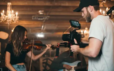 Un caméraman s'apprête à créer un clip vidéo, filmant une violoniste et un guitariste dans un décor chaleureux avec des lustres.