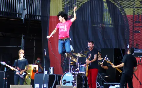 Un chanteur saute sur scène, micro en main, lors d'un concert en plein air. Le groupe joue avec énergie, une ambiance de festival.