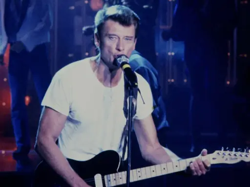 Johnny Hallyday chante en live, guitare à la main. On se demande combien gagne un musicien de Johnny Hallyday pour une telle performance.